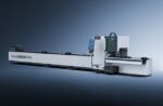 The דגם 6024T is a large, modern industrial tube laser cutting machine featuring a sleek white and black design, control panels, and an extended horizontal platform set against a gradient blue background.