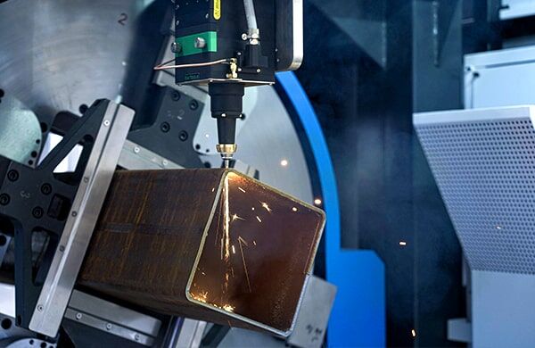 The דגם 9035NT laser cutting machine slices through a large, hollow metal square tube with bright sparks in an automated industrial setting.