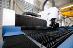 The דגם 3015N is a large, modern laser cutting machine featuring a spiked metal cutting bed and advanced industrial equipment in the background.