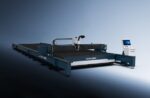 A large industrial laser cutting machine, דגם 24030TX by SENFENG, with a digital control panel and flat cutting bed, is showcased against a smooth gradient background with a modern design.
