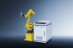 The דגם RC Series אנכי, a yellow industrial robotic arm, stands beside a white and blue control-panel machine against a gradient blue background.
