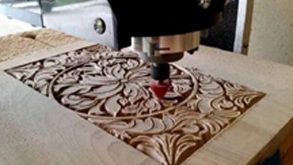 A CNC machine is carving an intricate floral and leaf pattern into a wooden surface, creating detailed and symmetrical decorative designs.