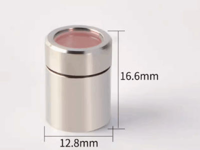 A חלון מגן RECI (D12.8 H16.6), a small cylindrical metallic object with a pink-tinted top, measuring 16.6 mm high by 12.8 mm wide, is shown against a plain white background.