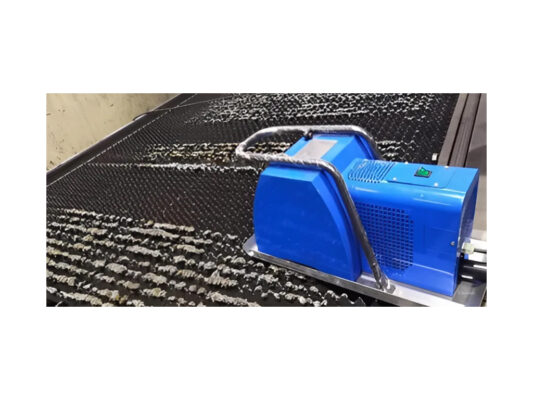 A blue industrial cleaning machine with a metal handle is positioned on a black, ribbed surface, likely cleaning residue or buildup from the material.