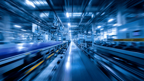 A blurred, fast-moving view of a modern, brightly lit factory interior, featuring automated machinery, conveyor belts, and industrial equipment in a blue-toned color scheme.